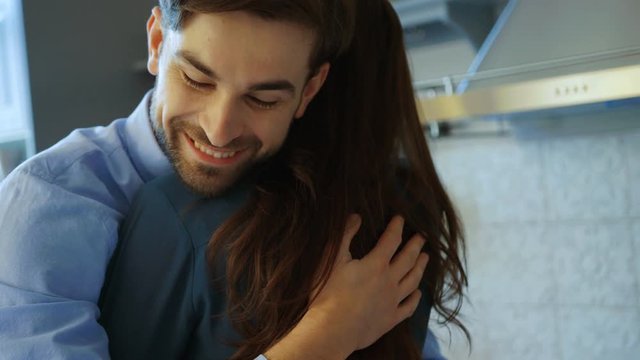 Close up of young lovely couple hugging each other in the kitchen. Smiling man. Indoors