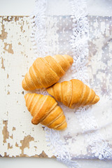 Beautiful and delicious croissants on the background of old laces and white table.