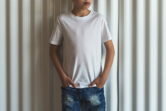Front view. Young hipster boy in sunglasses dressed in white t-shirt is stands indoor against white wall. Mock up. Space for logo, text, image.