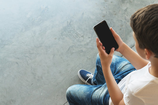 View from above. Boy in white T-shirt and sunglasses sitting indoor and uses smartphone. Teenager plays computer games on digital gadget, surfing internet. Social networks, computer games, e-learning.