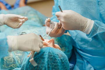 Male old professional dentist surgeon in uniform and female assistant helps to performing operation install dental implant teeth of woman patient in clinic light office with modern tools equipment.