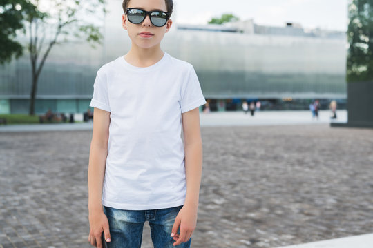 Front view. Young hipster boy in sunglasses dressed in white t-shirt is stands outdoor. Mock up. Space for logo, text, image.