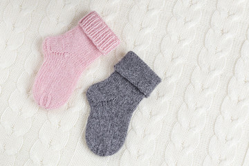 A pair of cute small different colored cashmere knitted newborn baby socks on a white woolen background