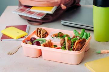 Open lunchbox met gezond voedsel op tafel in de buurt van rugzak, laptop en thermomok