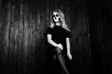 Halloween skull make up girl wear in black against wooden wall at studio.