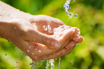 Woman washing hand outdoors. Natural drinking water in the palm. Young hands with water splash, selective focus