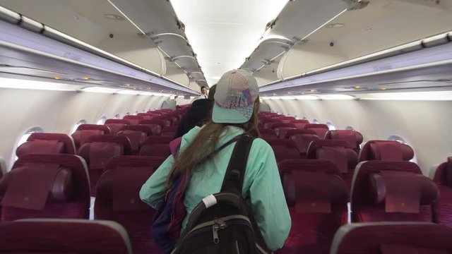 Girl go through rows of seats in the airplane to their seats. Aircraft cabin with rows of seats. Interior passengers airplane with people on seats. Passengers traveling by a modern commercial plane