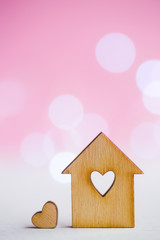 Obraz na płótnie Canvas Wooden house with hole in form of heart with little heart on pink bokeh background