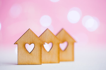 Obraz na płótnie Canvas Three wooden houses with hole in form of heart on pink bokeh background
