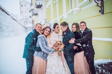 Bridesmaids and groomsmen dressed in powder dress tones surround stylish wedding couple in winter...
