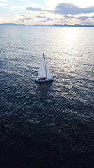 Fototapeta premium Aerial drone bird's eye view of yacht cruising near small islet of Ydrousa at sunset with beautiful scattered clouds, Voula, Athens riviera, Attica, Greece