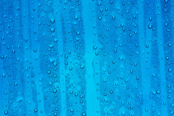 Fototapeta na wymiar Regentropfen auf Glasscheibe mit Himmelblauem Grund