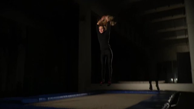 A slender woman in tight clothes jumps on a trampoline and does a somersault, slow motion