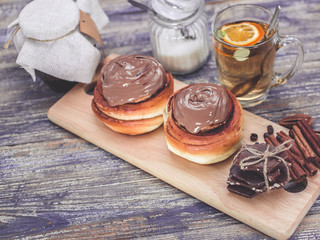 Cinnamon buns and chocolate, herbal tea. Composition on a wooden background. Selective focus. Easy toning