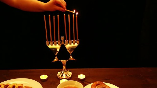 a woman holds a burning candle in her hand with which she lights candles in a candlestick for the Hanukkah. a woman lights candles from the first candle from right to left. the candlestick 