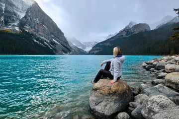 Woman sitting on rock in Lake Louise and enjoying the view of Victoria Glacier. Canadian Rockies....