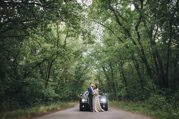 Newlyweds near the wedding car surrounded by summer forest.