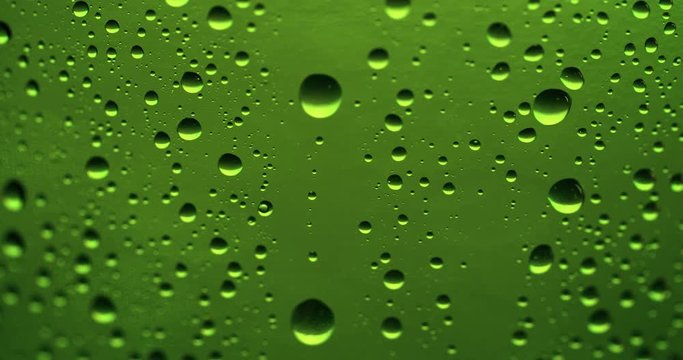 Drop of condensate drips on beer bottle glass 4k extreme close-up video. Water drops falling down on green background
