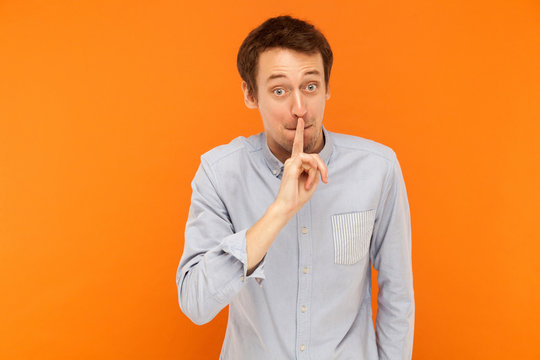 Shh, it's secret! Businessman holding finger near mouth and looking at camera with big shocked eyes.