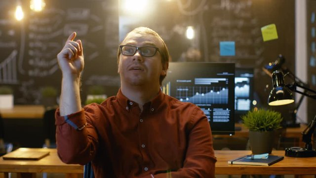 Young Office Worker Has Eureka Moment While Sitting in His Office Thinking, Bulb Over Him Lights Up When He has an Idea, He Turns and Starts Working on His Personal Computer. RED EPIC-W 8K Camera.