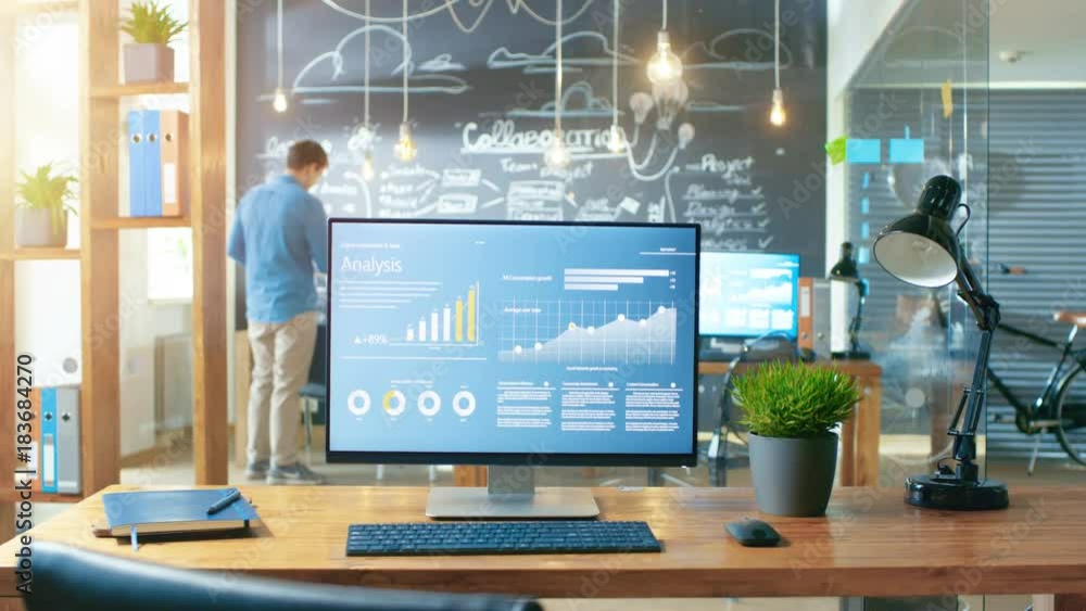 Poster Personal Computer with Mobile Application Design Showing on the Monitor Stands on the Office Desk, In the Background Man Working in the Daytime Office Environment. RED EPIC-W 8K Camera.