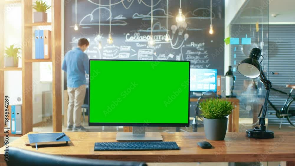 Poster personal computer with mock-up green screen monitor stands on the office desk, in the background man