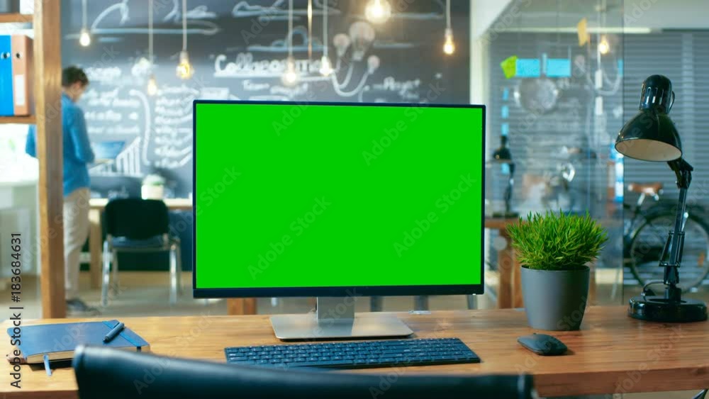Poster personal computer with mock-up green screen monitor stands on the office desk. in the background man