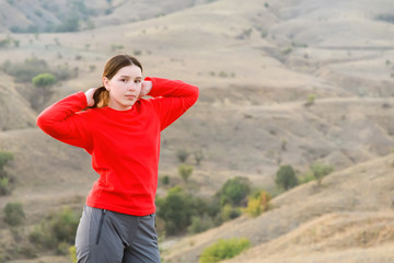 Fototapeta na wymiar The girl in the steppe mountains in a red fleece jacket and Hiking pants straightens hair tail