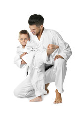 Little boy with instructor practicing karate on white background