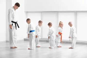 Foto op Plexiglas Vechtsport Kleine kinderen en instructeur die rituele buiging uitvoeren voorafgaand aan het beoefenen van karate in dojo