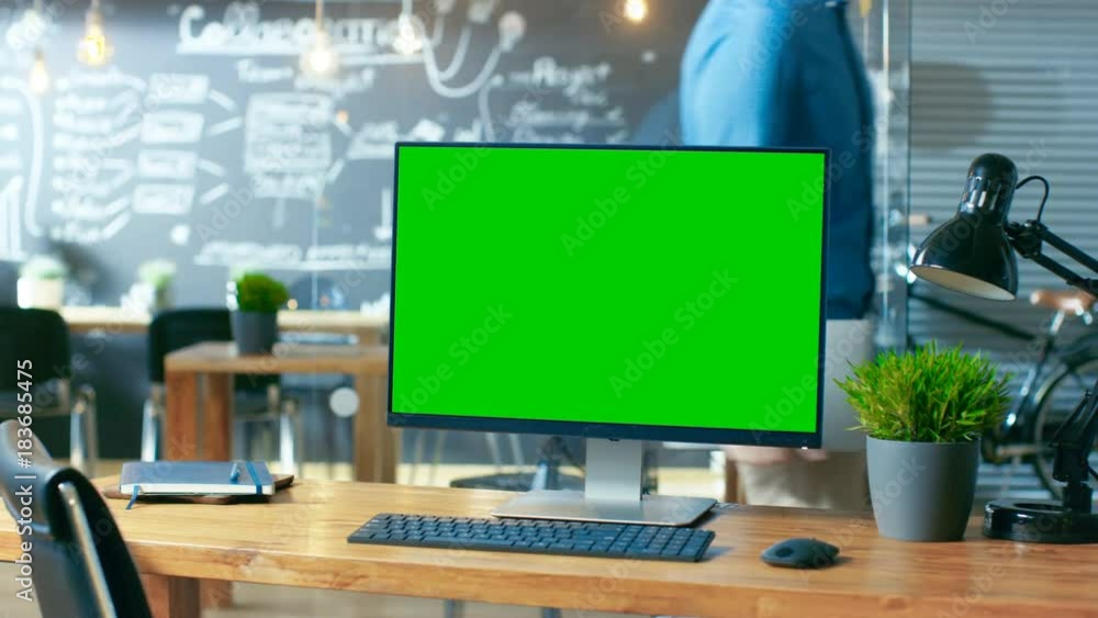 Poster personal computer with mock-up green screen monitor stands on the office desk, in the background man