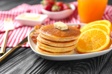 Plate with yummy pancakes and orange on wooden table