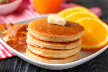 Plate with yummy pancakes, orange and fried bacon on wooden table
