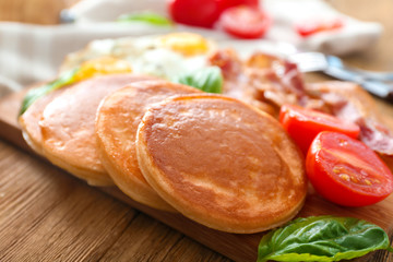 Board with yummy pancakes, tomatoes and fried bacon on wooden table