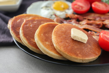Plate with yummy pancakes, tomatoes, fried egg and bacon on table