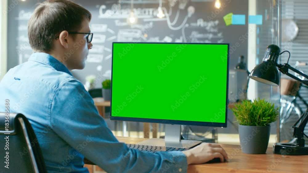 Poster young man works at his desk on the personal computer with mock-up green screen. in the background hi