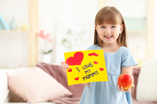 Little girl holding greeting card and apple for Mother's day at home