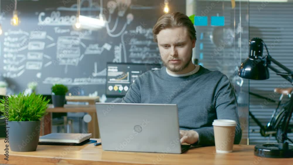 Poster Handsome Young Office Employee Thinks on a Problem Solution While Typing on a Laptop Computer. He's Working in the Creative Stylish Office.