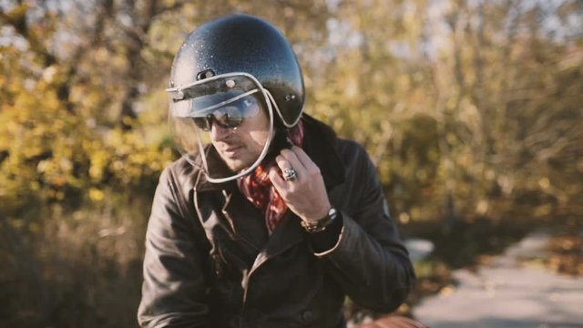 a man motorcyclist takes off his helmet in slow motion. Autumn background 