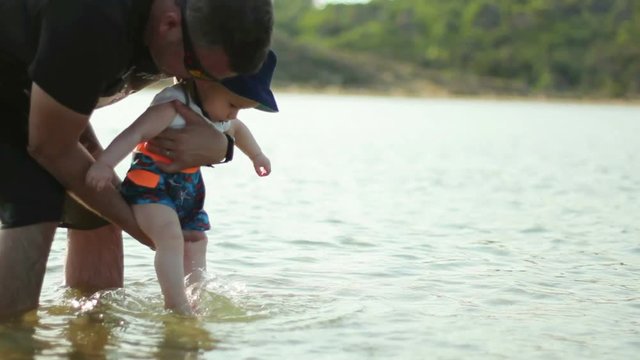 Little baby splashing water by the feet in father hands at beach
