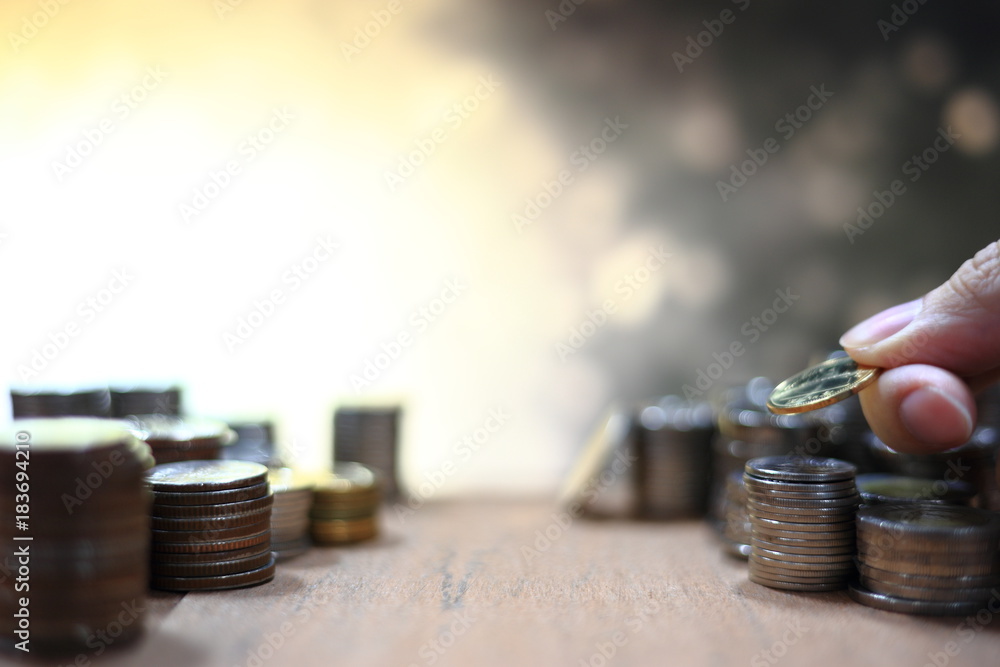 Poster hand holding and arranging coin into stacking pile column on lighting golden yellow bokeh background
