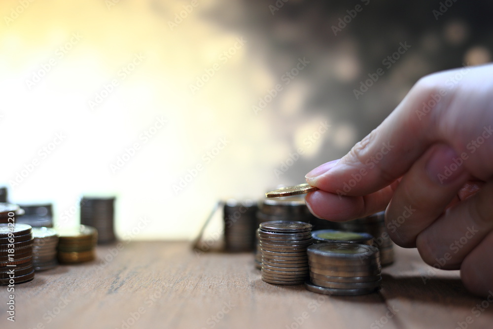 Poster hand holding and arranging coin into stacking pile column on lighting golden yellow bokeh background