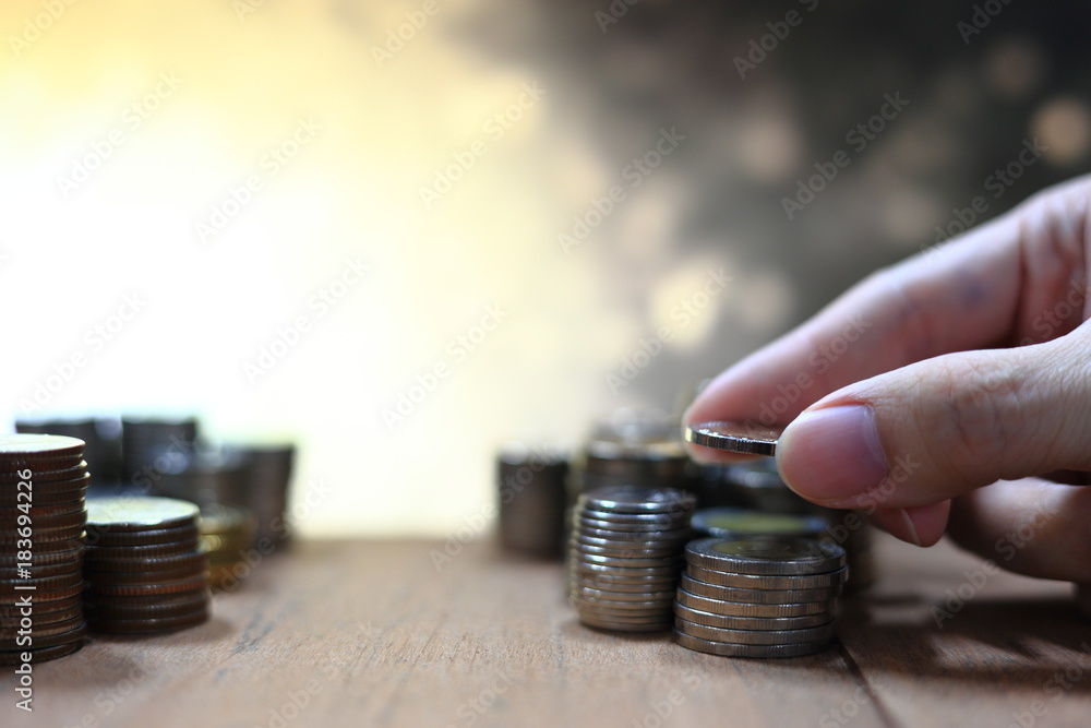 Poster hand holding and arranging coin into stacking pile column on lighting golden yellow bokeh background
