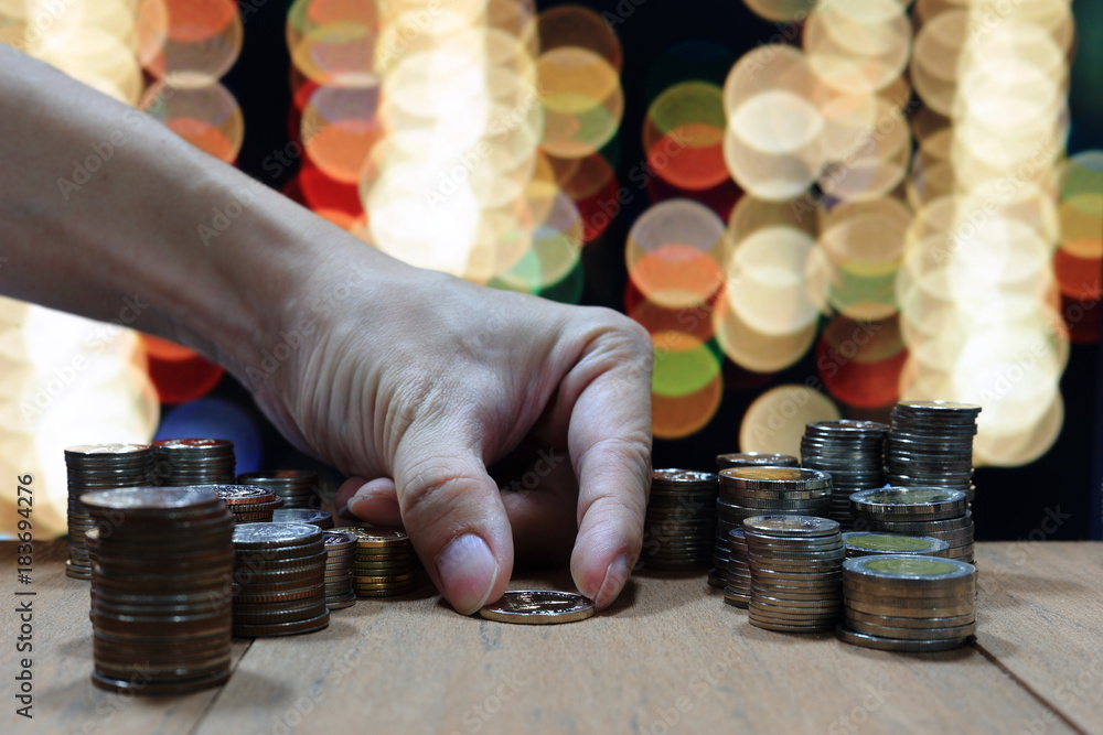 Poster hand holding and arranging coin into stacking pile column on lighting bokeh background