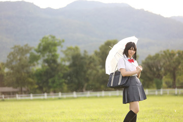 Japanese school with umbrella on rain in countryside with grass mountain and tree