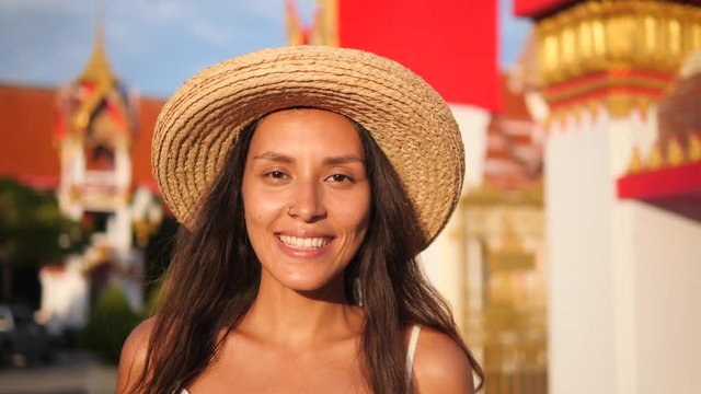 Portrait of Attractive Young Mixed Race Tourist Girl in Straw Hat with Traditional Thai Buddhist Temple on Background. Thailand. 4K, Slowmotion.