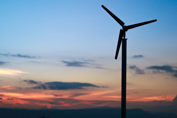 A solitary Wind Turbine silhouetted against a dramatic sunset sky twilight time.