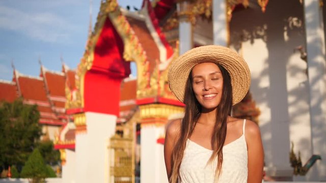 Portrait of Beautiful Smiling Young Mixed Race Tourist Woman in Straw Hat with Traditional Thai Buddhist Temple on Background. Thailand. 4K, Slowmotion.