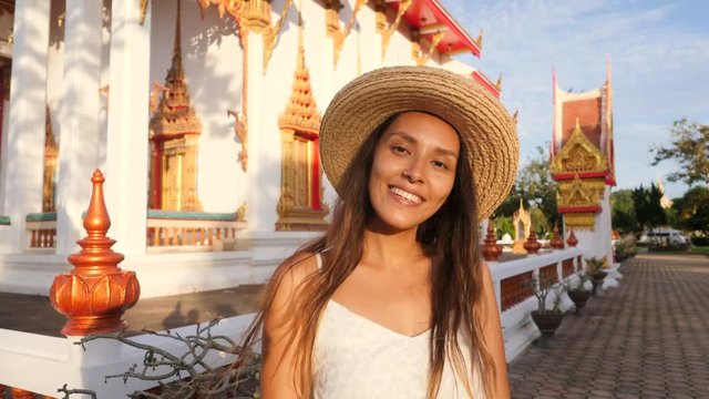 Portrait of Smiling Attractive Young Mixed Race Hipster Tourist Girl in Straw Hat with Traditional Thai Buddhist Temple on Background. Thailand. 4K, Slowmotion.