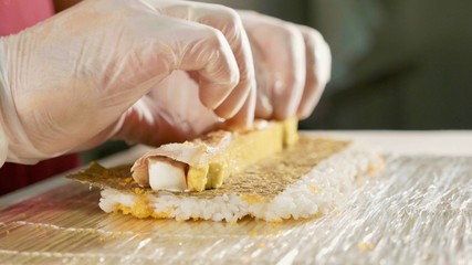 Professional sushi chef preparing roll at commercial kitchen, close-up.